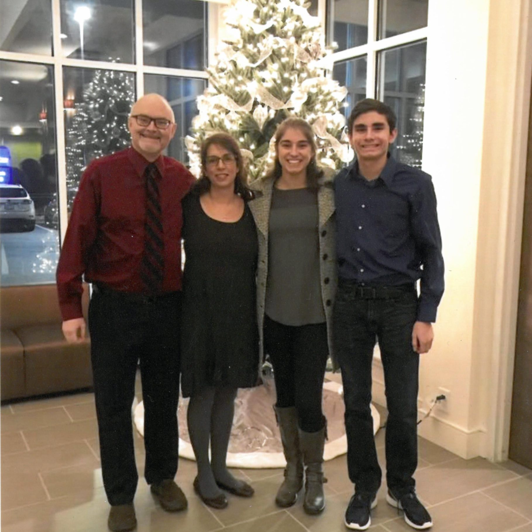 Family of four smiling in front of Christmas tree