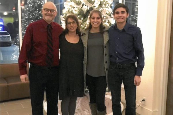Family of four smiling in front of Christmas tree